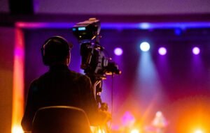 A videographer recording a live concert with vibrant spotlights, using professional equipment.